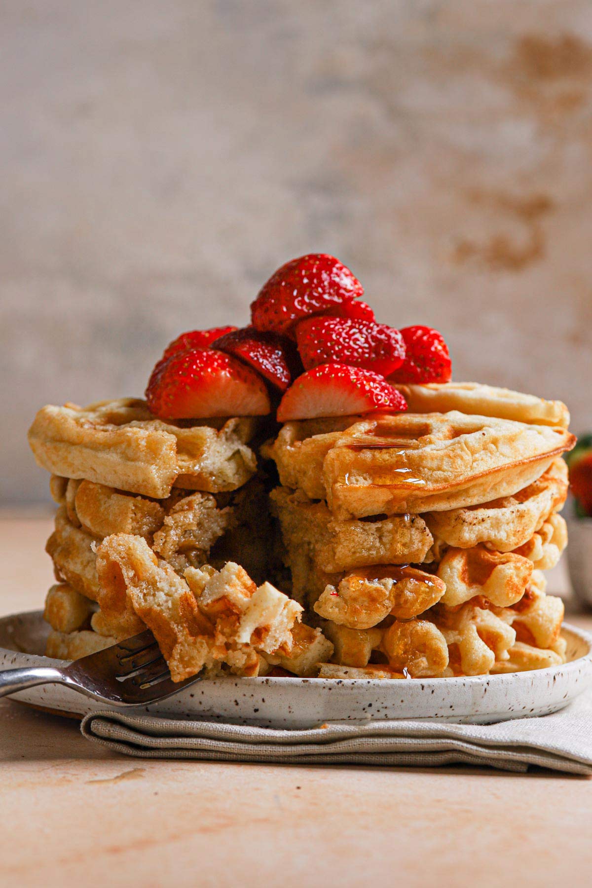 Stack of Belgian waffles with fork cut into them and strawberries on top.