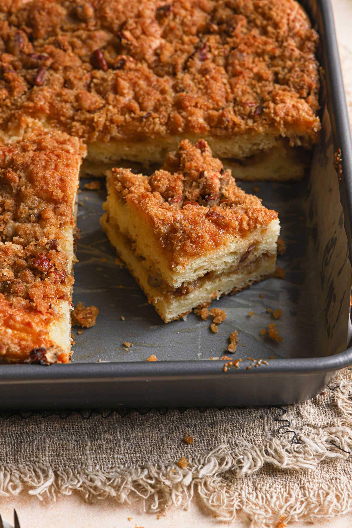 Coffee cake in a pan with a single slice cut away from the whole cake.