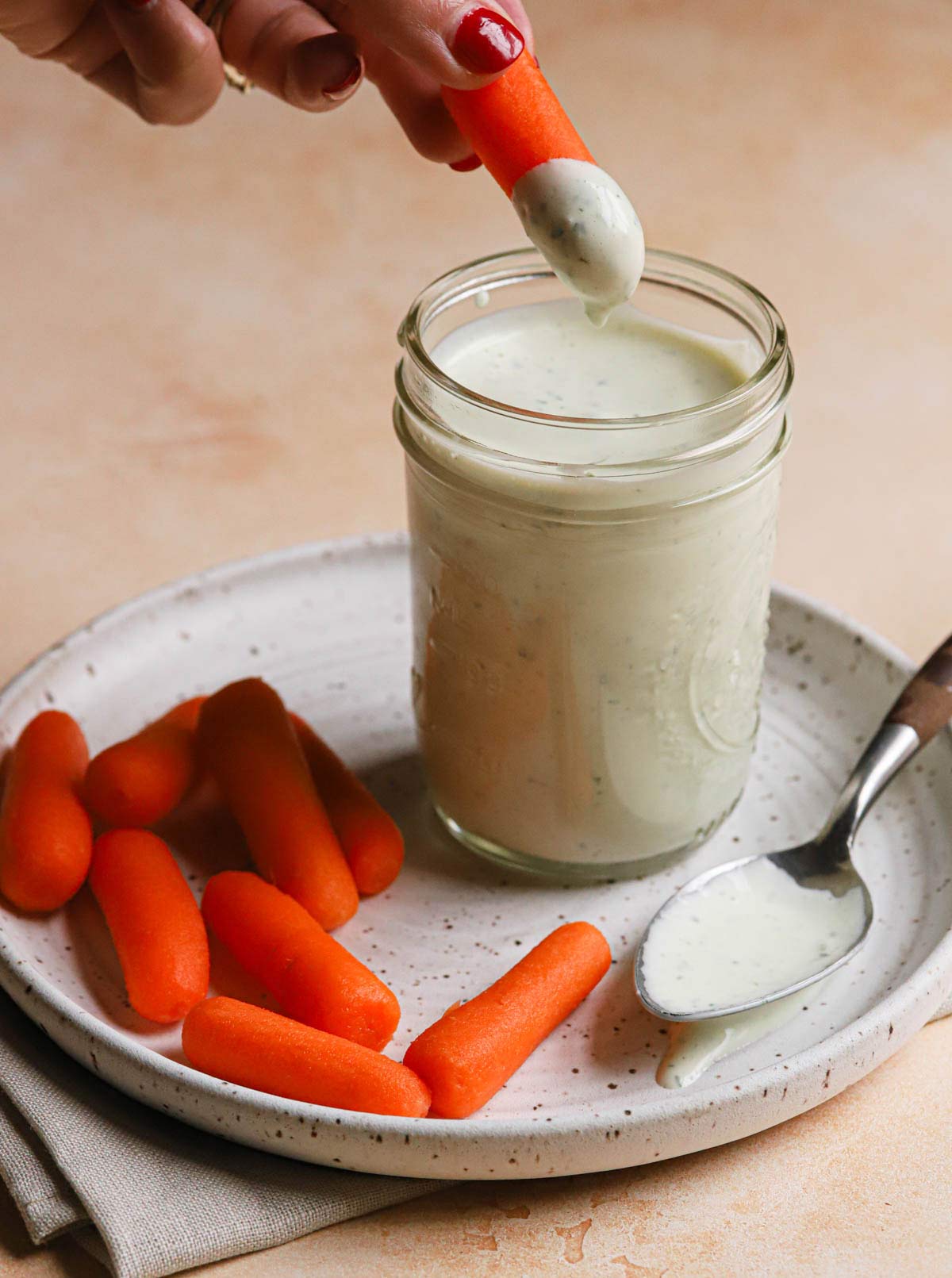 A baby carrot being dipped into a jar of homemade ranch dressing.