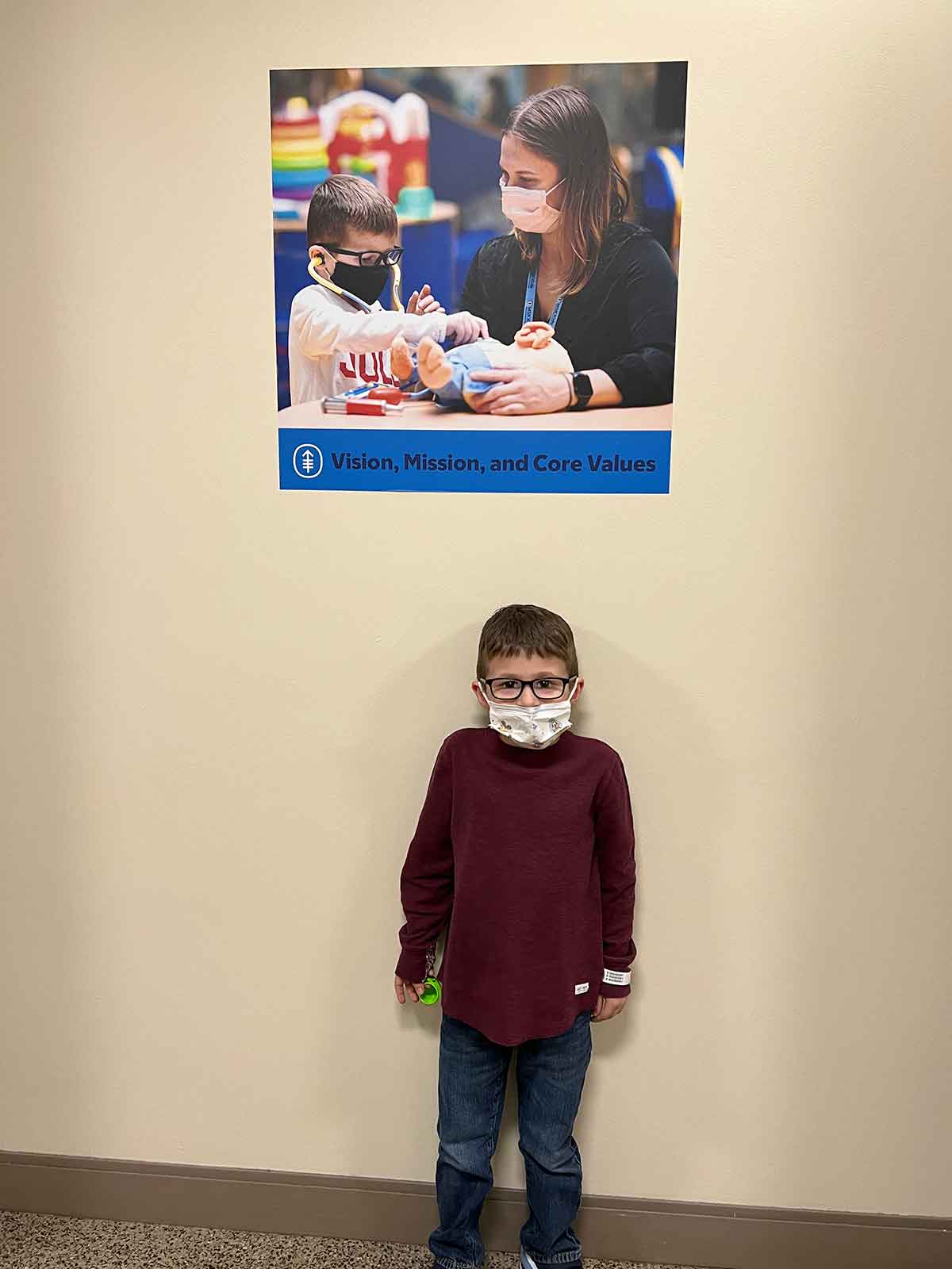 Boy standing beneath a poster of child life specialist working with a little boy.