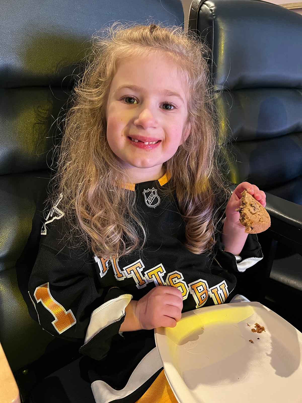 Girl in a hockey jersey eating a chocolate chip cookie.