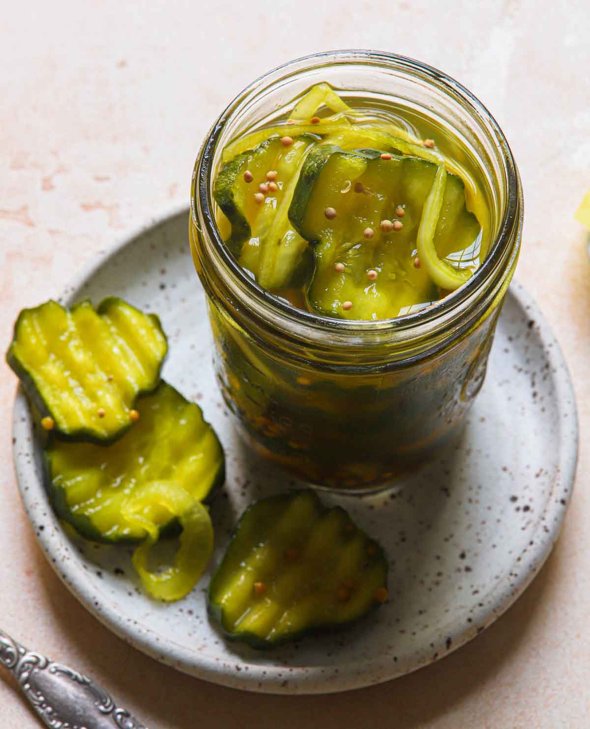 Open jar of bread and butter pickles on a plate with three pickle slices in view.