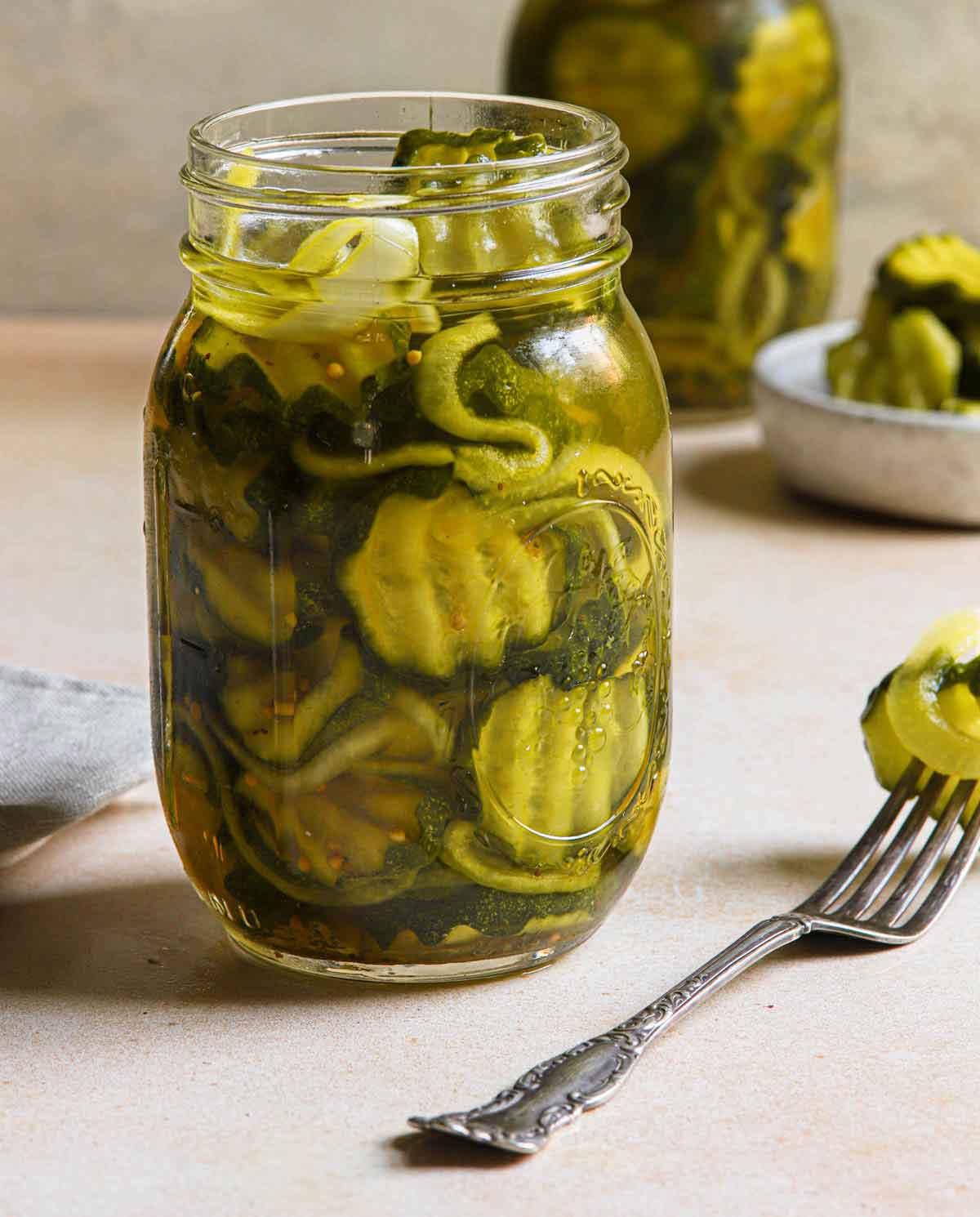 Jar of bread and butter pickles next to fork with a pickle on it.
