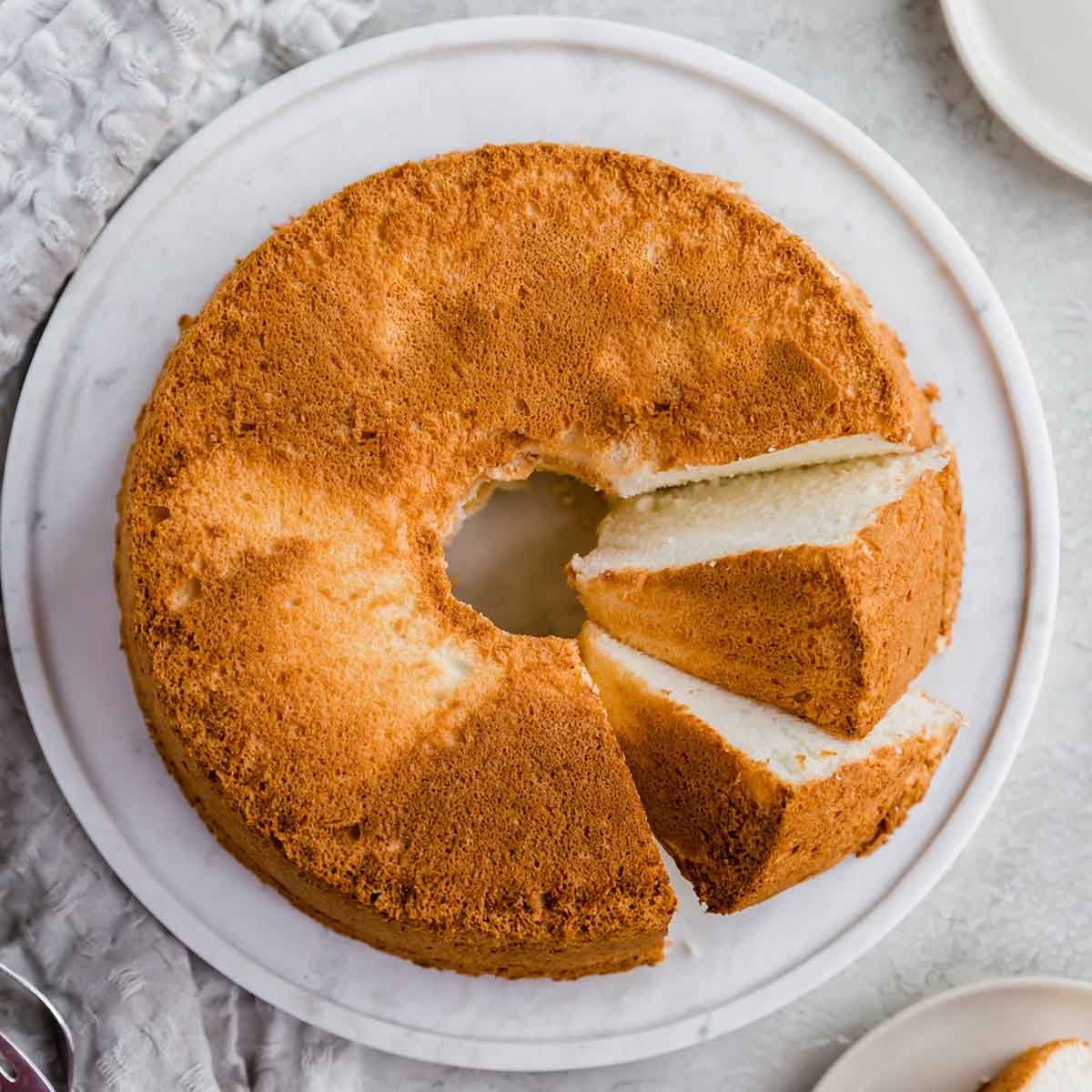 A baked angel food cake on a serving plate with two slices cut and laying on side.