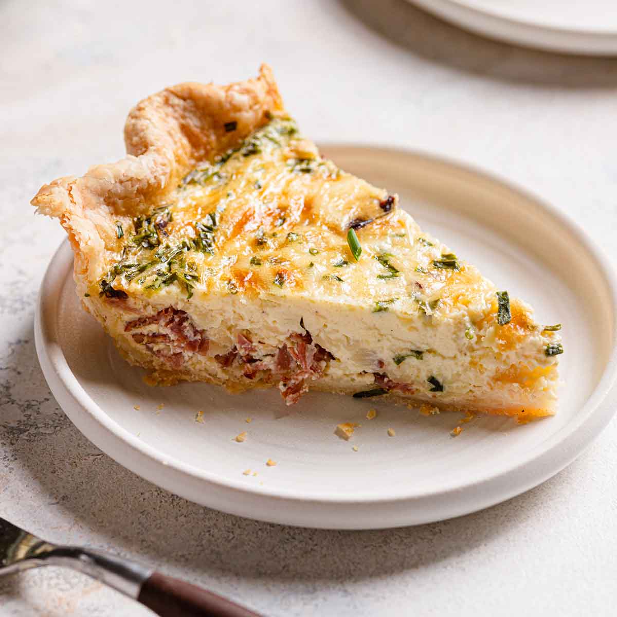 Side view of a slice of quiche on a white plate.