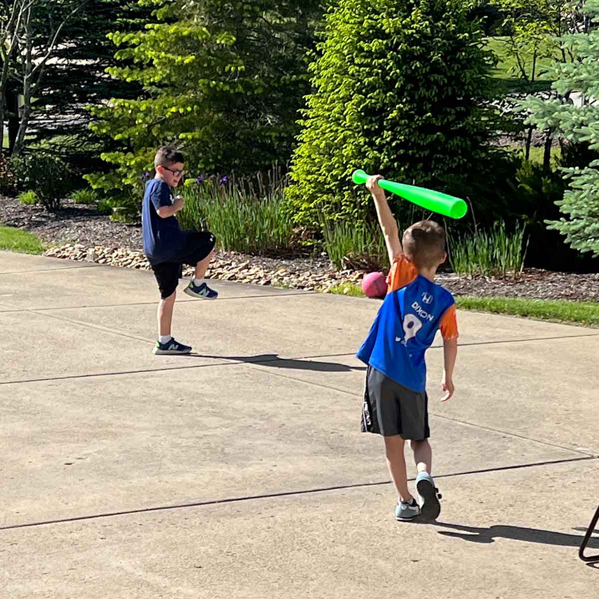 Boys playing baseball in a driveway.