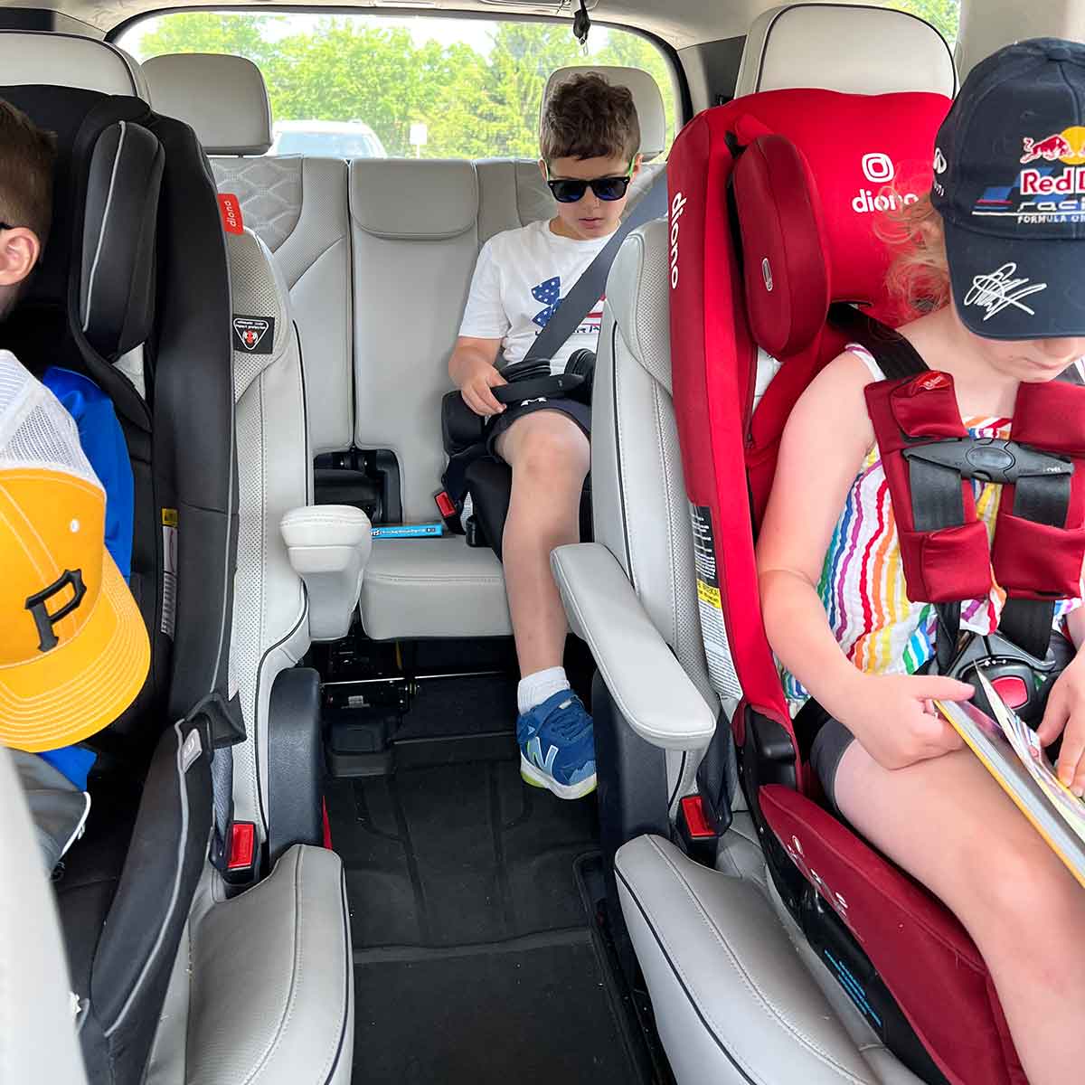 Three kids in car seats in the back of a car.