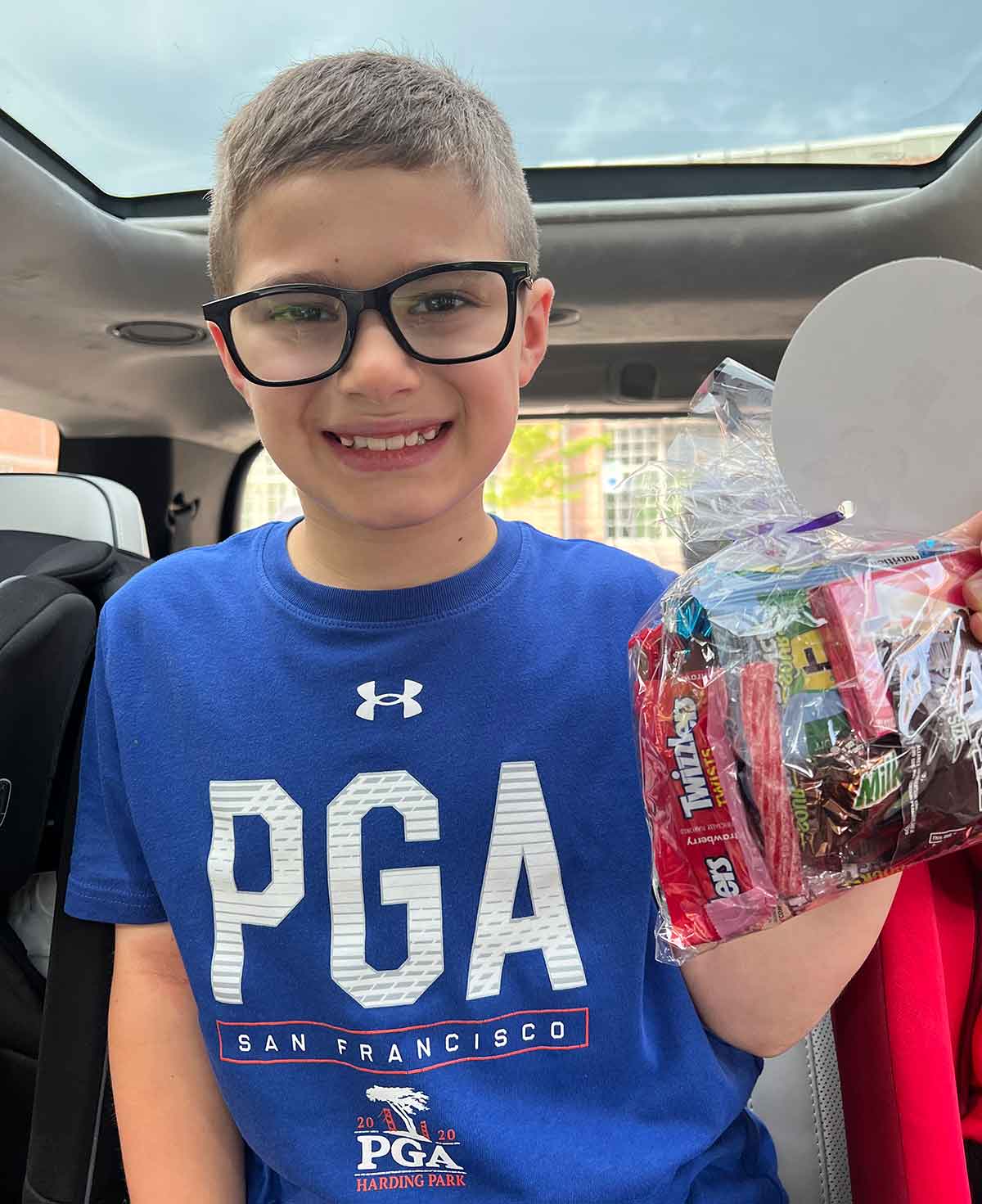 Boy in glasses and blue tshirt smiling and holding a bag of candy.