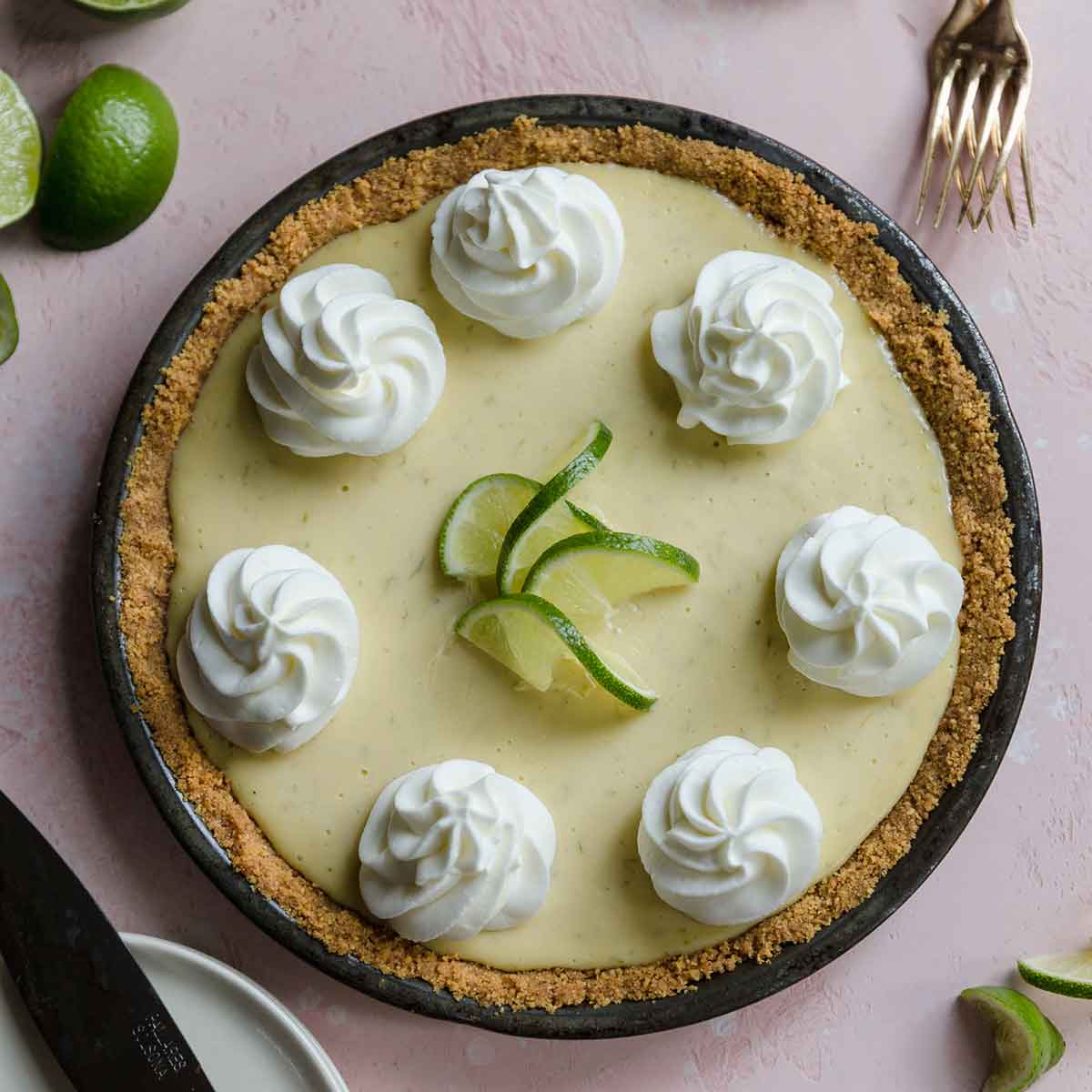 Overhead photo of baked key lime pie adorned with dollops of whipped cream and lime slices.