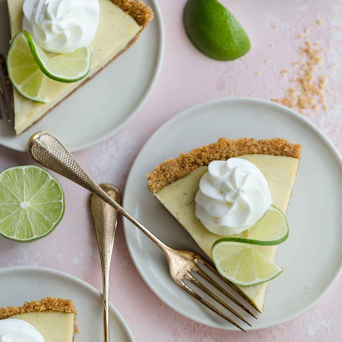 Slices of key lime pie on plates with dollops of whipped cream and lime slices.