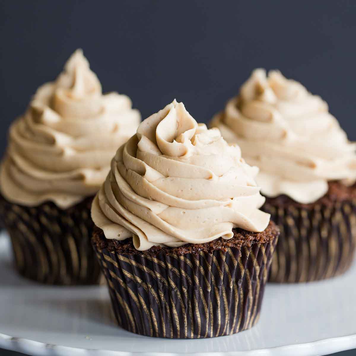 Mocha cupcakes with espresso frosting in dark paper liners on a white serving plate.