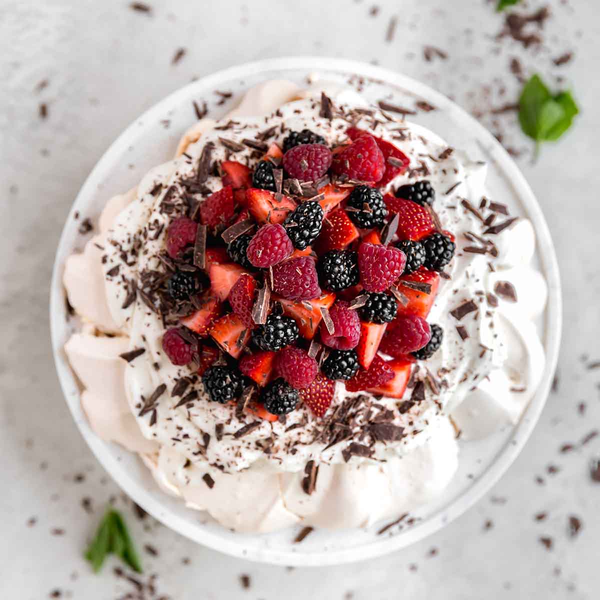 Overhead photo of pavlova topped with whipped cream, fresh berries, and chocolate shavings.