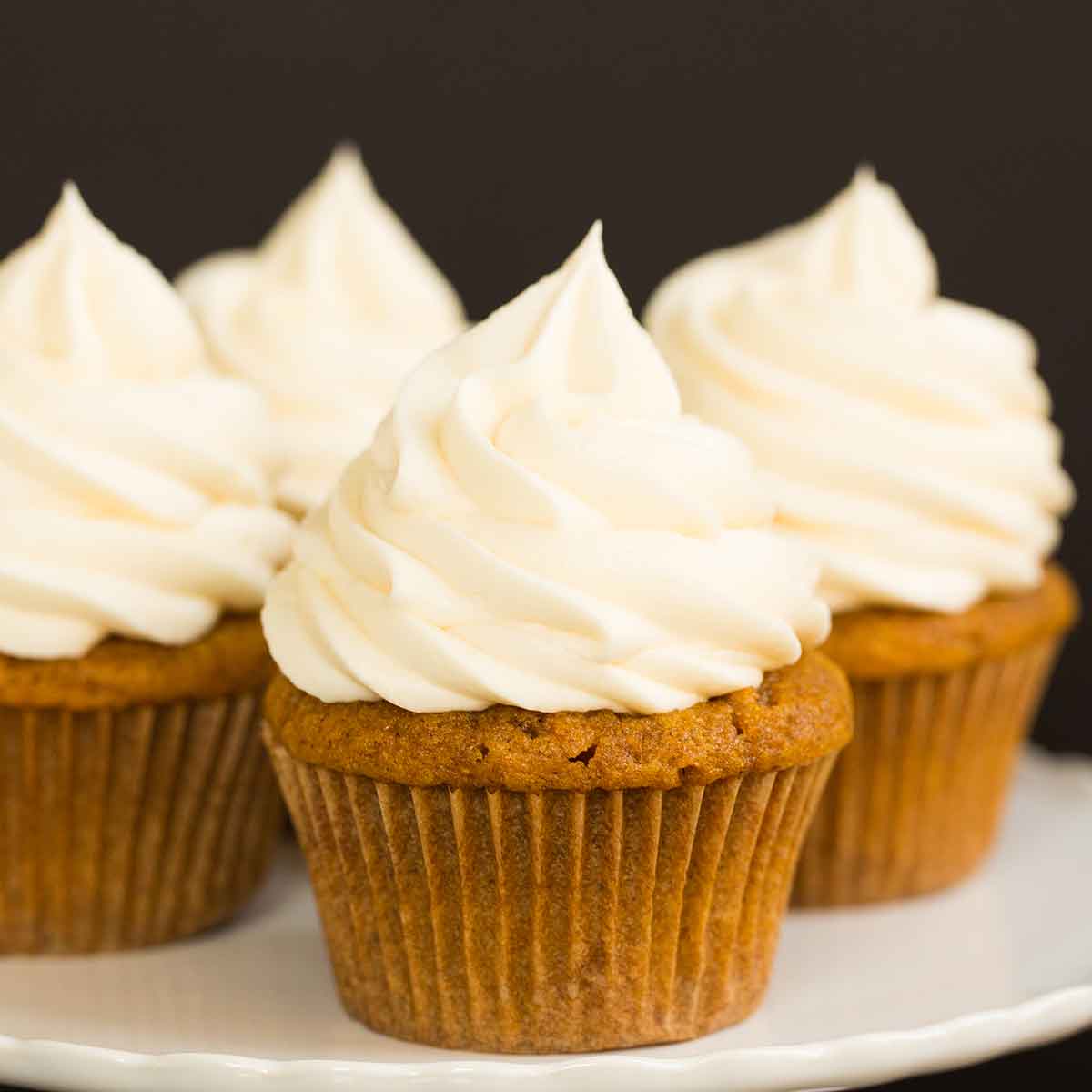Pumpkin cupcakes topped with swirls of cream cheese frosting on a white serving plate.