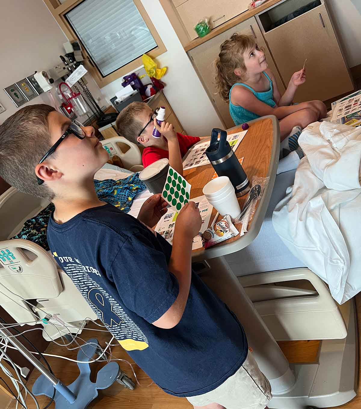 Three kids sitting around a hospital bed playing bingo.