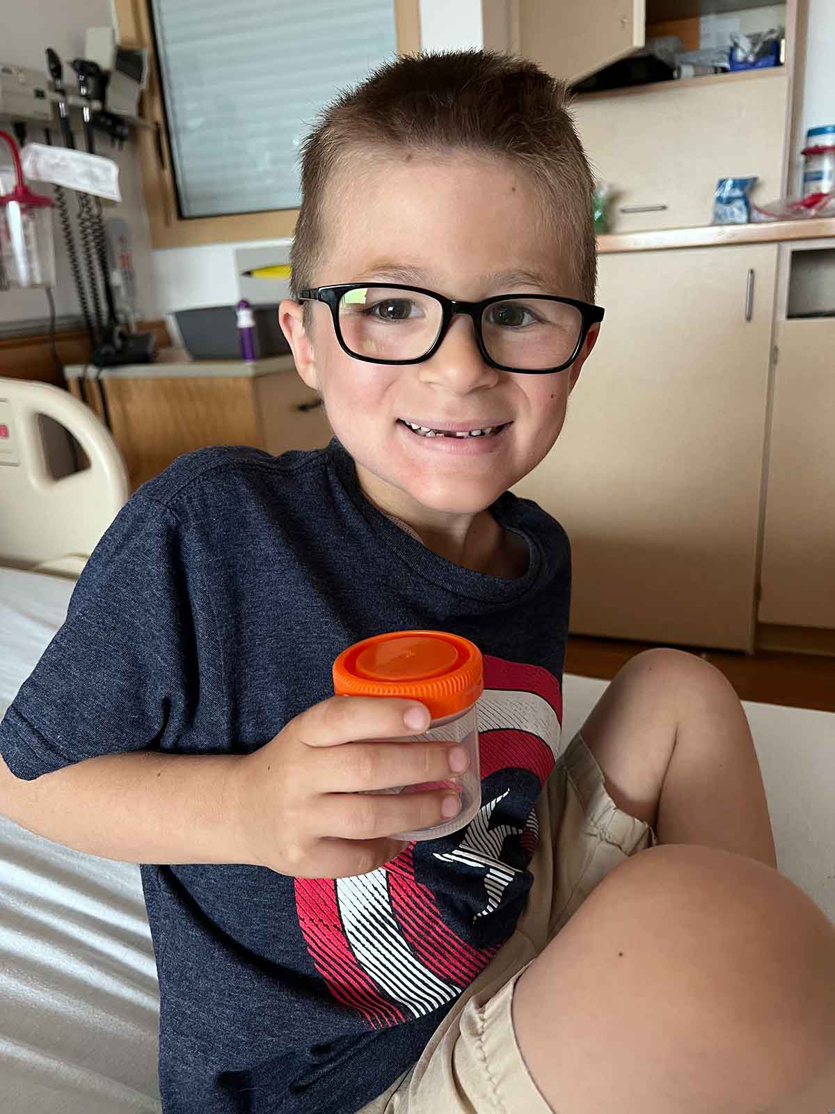 Little boy sitting in a hospital bed holding a cup.