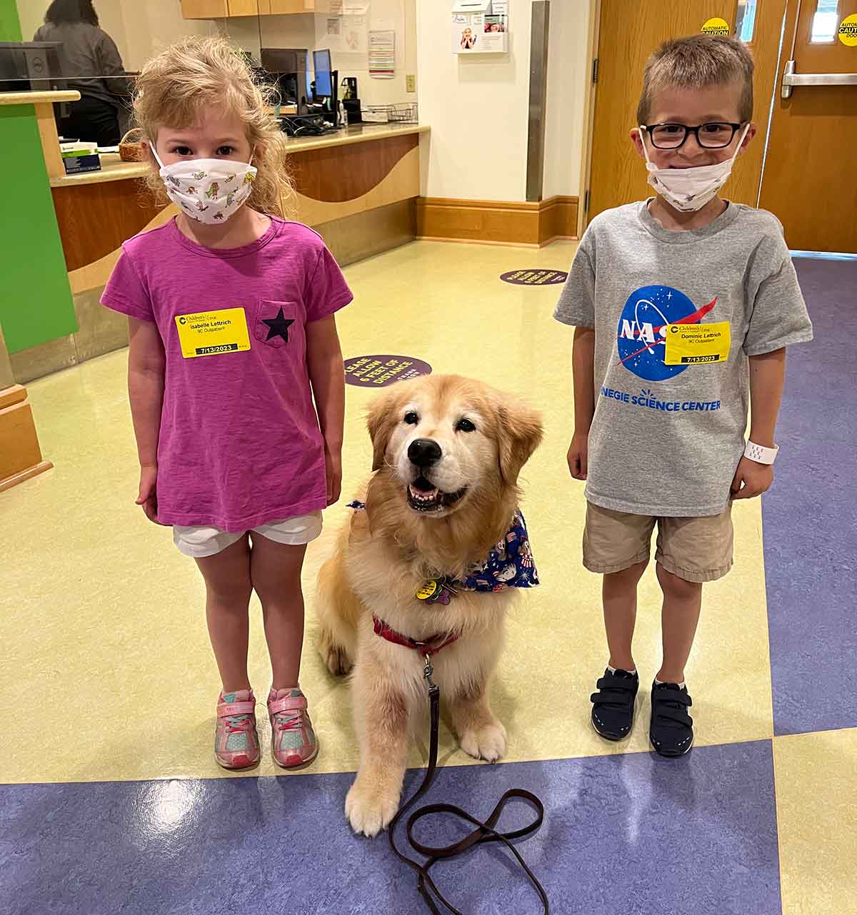 A girl and a boy posing for a photo with a Golden Retriever dog sitting between them.