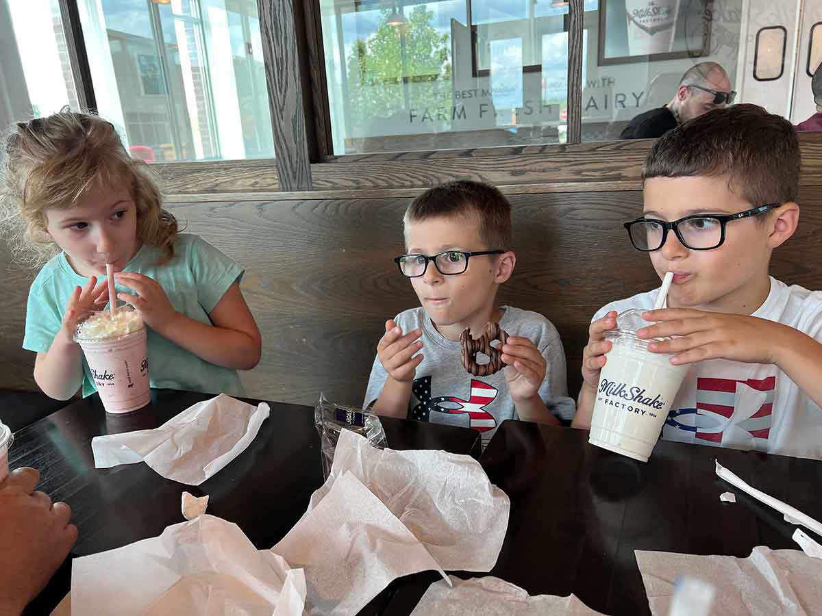 One girl and two boys sitting in a booth drinking milkshakes.