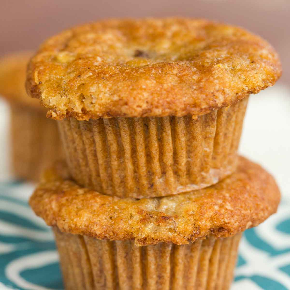 Two banana muffins stacked on top of each other on a teal and white dish towel.