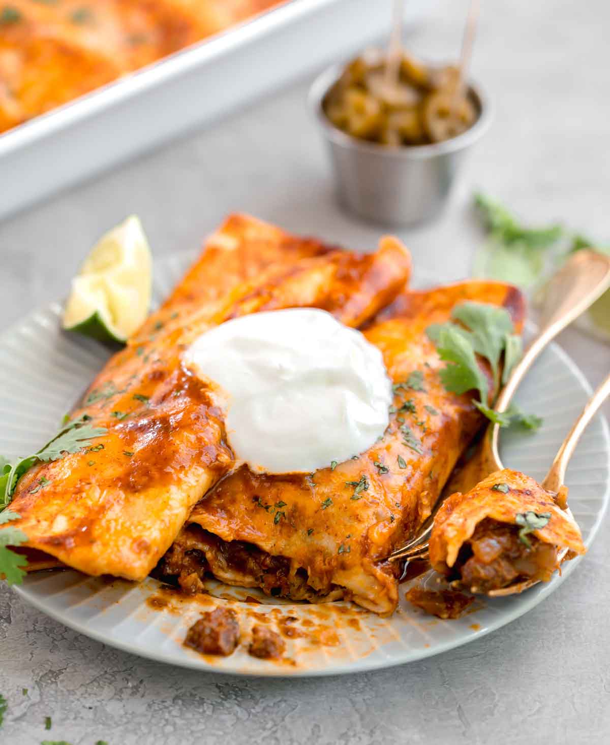Two beef enchiladas on a plate with a dollop of sour cream on top.