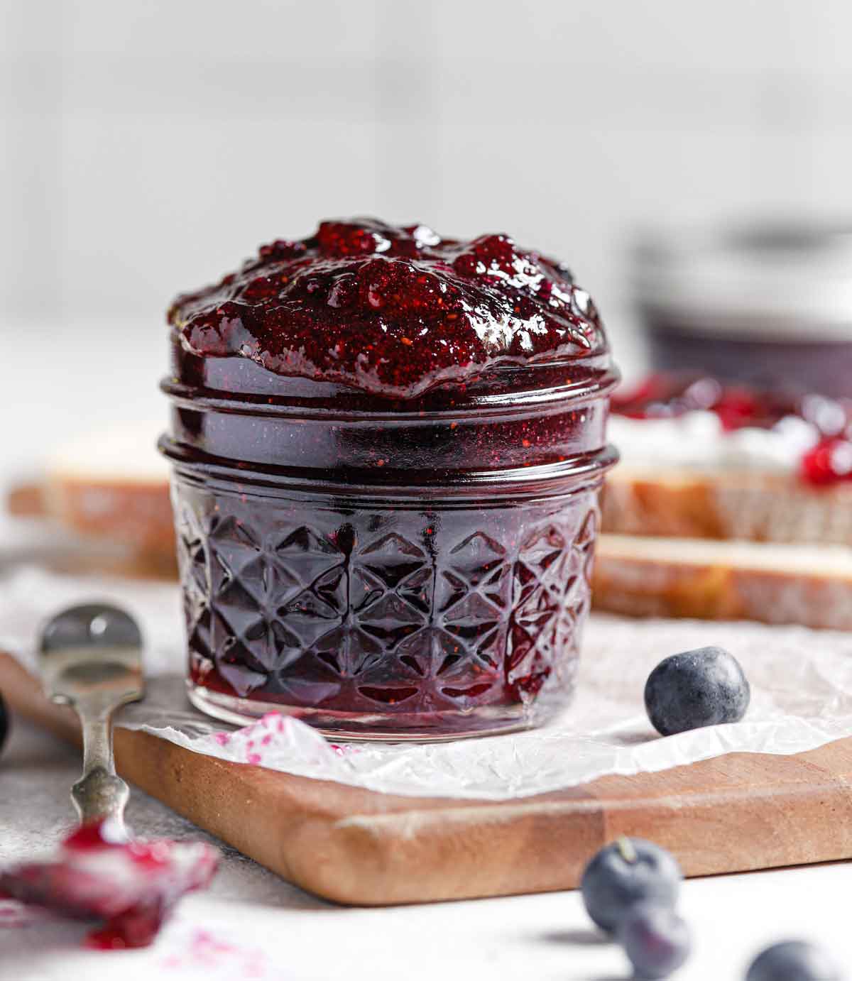 Glass jar with blueberry jam overflowing over the top.
