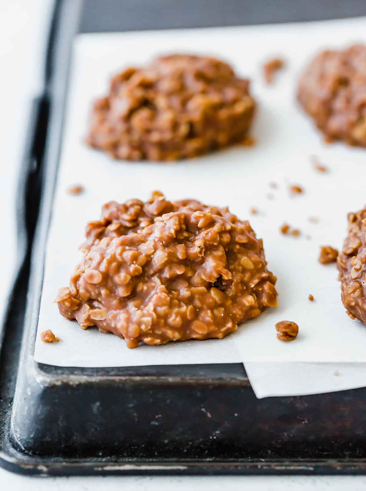 No bake cookies lined up on parchment paper that has been placed on an upside down baking sheet.