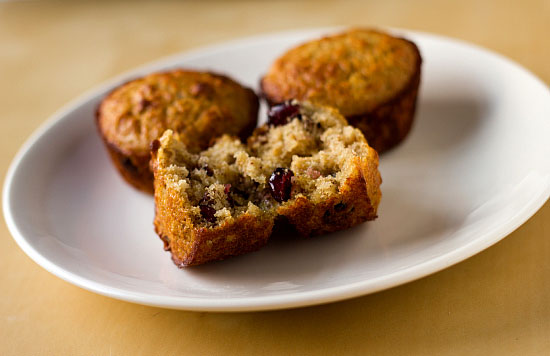 A broken open oatmeal muffin with cranberries, dates, and pecans on a plate with two other muffins.