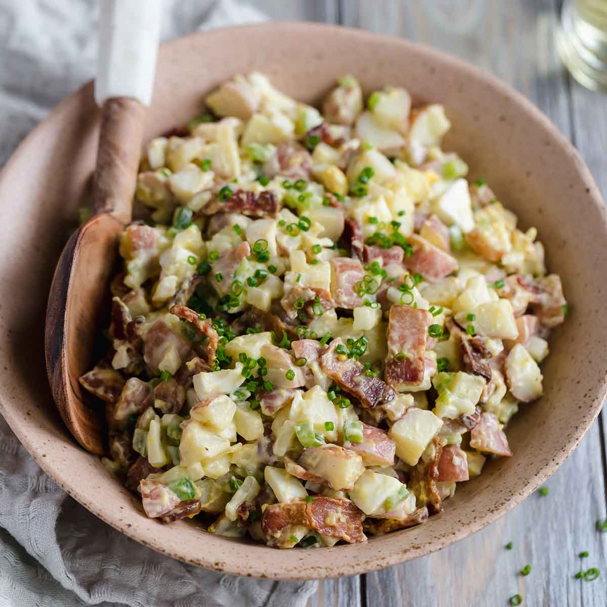 Potato salad with bacon and hard boiled eggs in a bowl with a serving spoon.