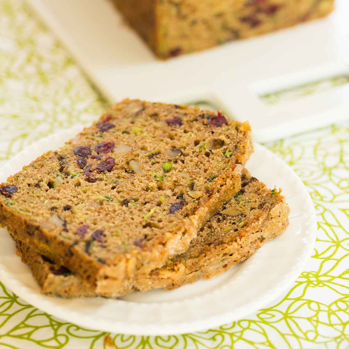 Two slices of spiced zucchini bread with walnuts and dried cranberries stacked on a white plate.