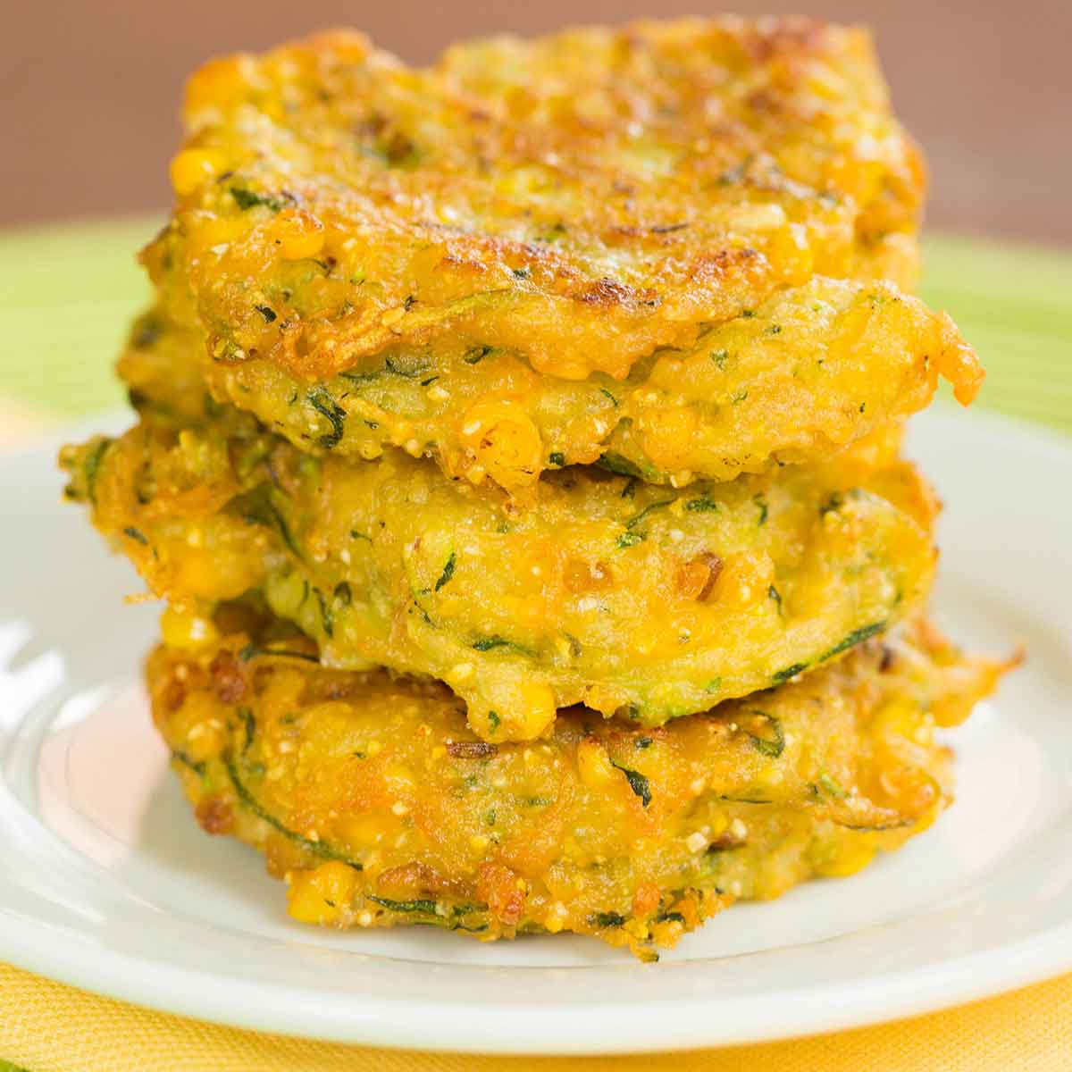 A stack of three zucchini corn fritters on a white plate.