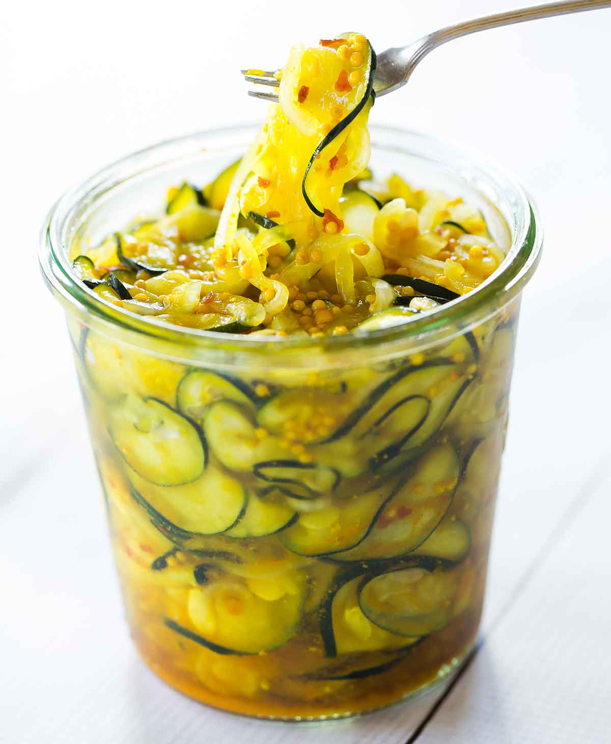 A fork lifting zucchini pickles out of a glass jar.