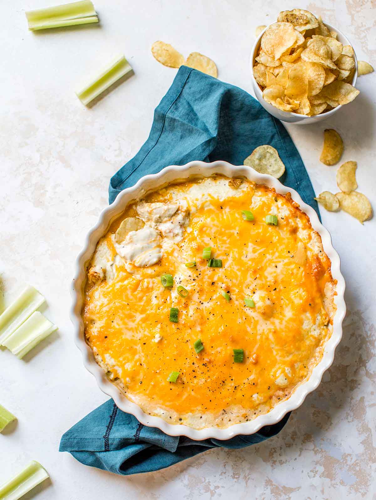 Buffalo chicken dip in a round white baking dish with potato chips and celery nearby.
