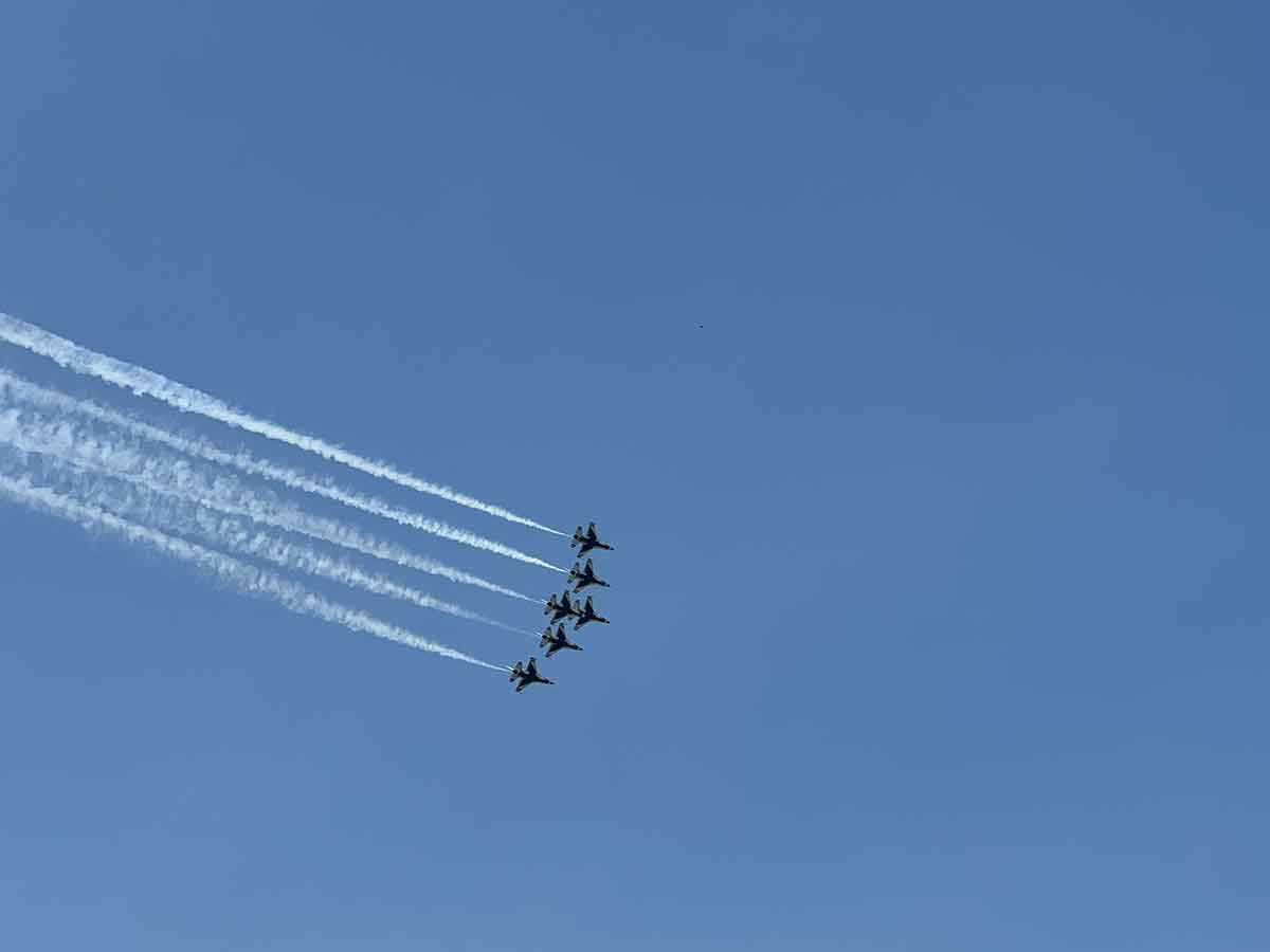 Blue sky with six fighter jets flying from left to right with smoke coming out the back.