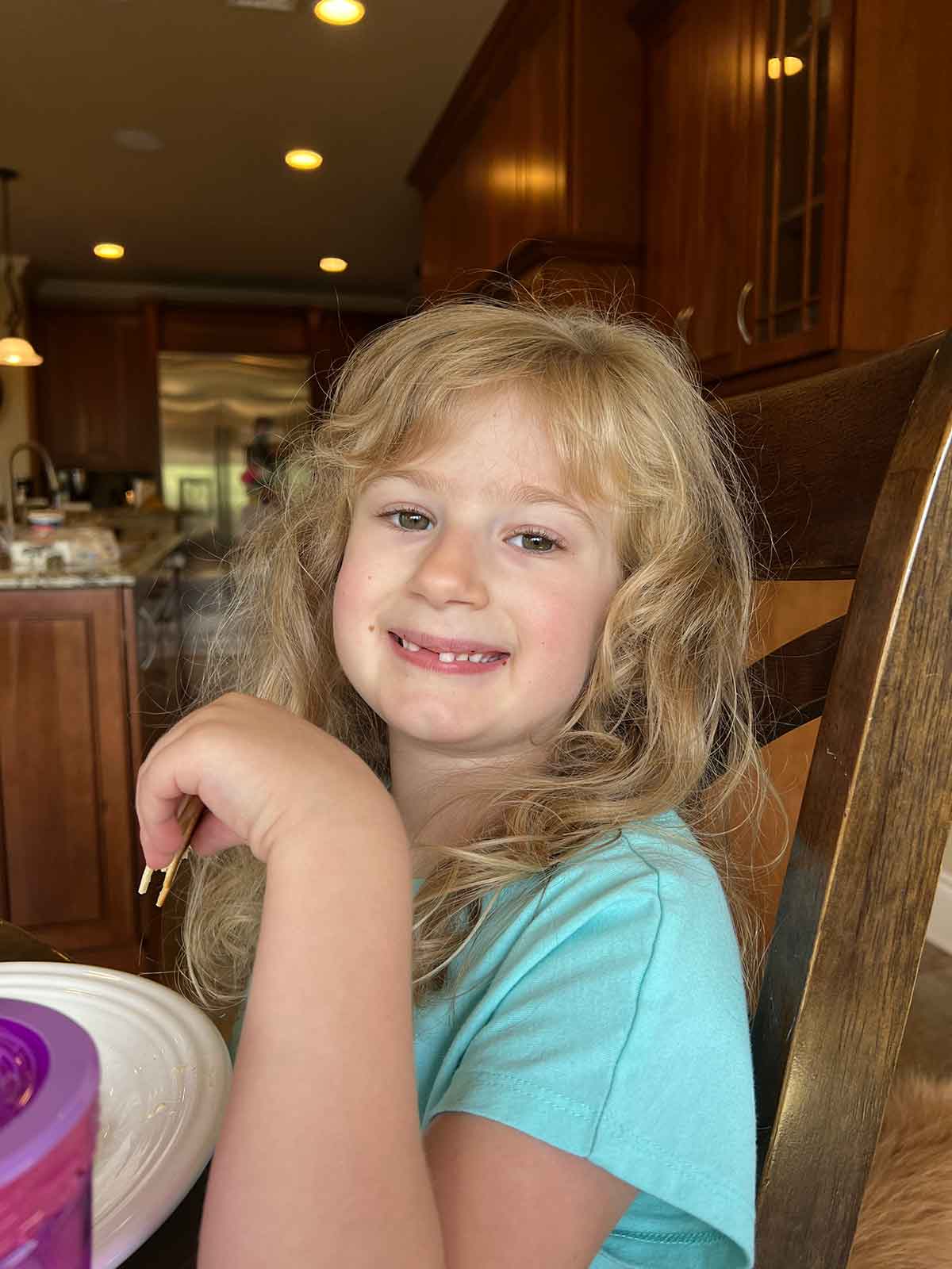 Little girl sitting in a kitchen chair smiling at the camera.