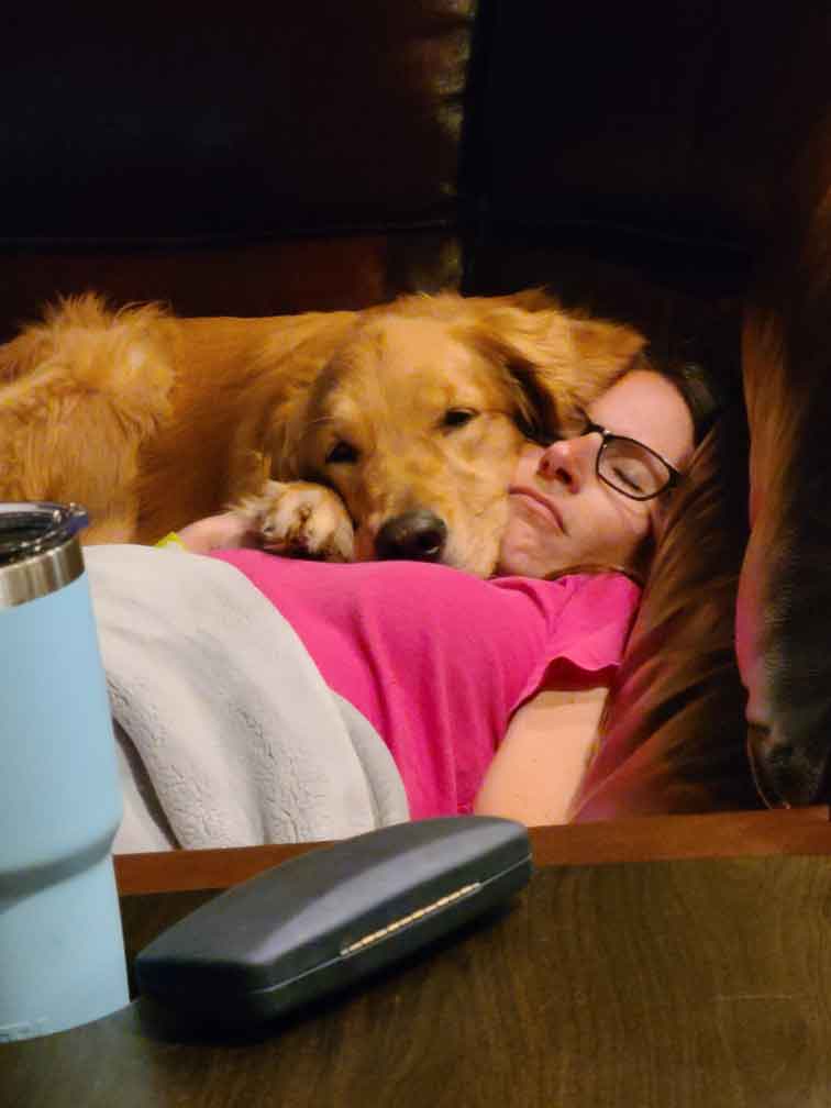 Dog laying on top of woman in glasses sleeping on couch.