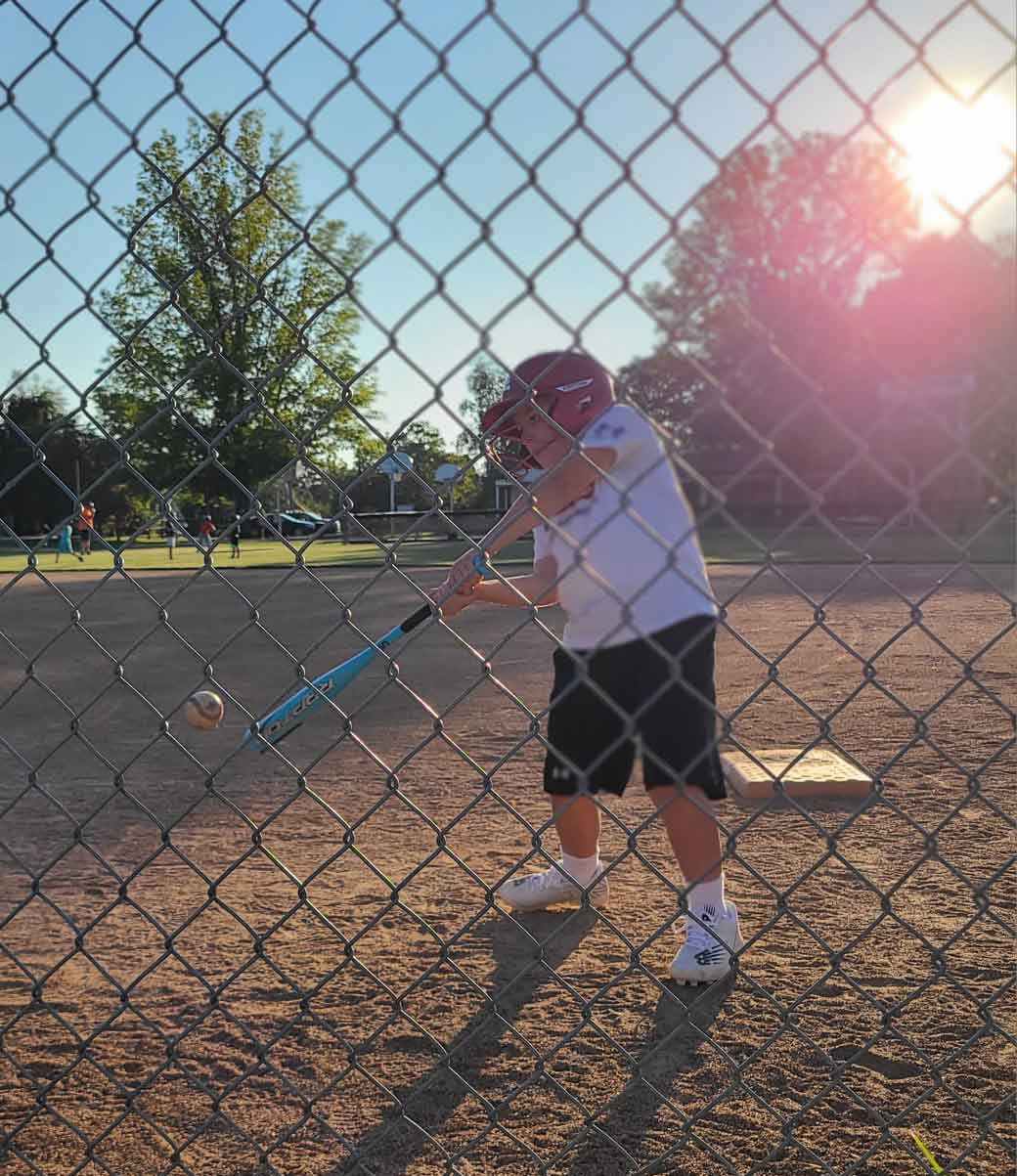 Boy hitting a baseball towards a fence.