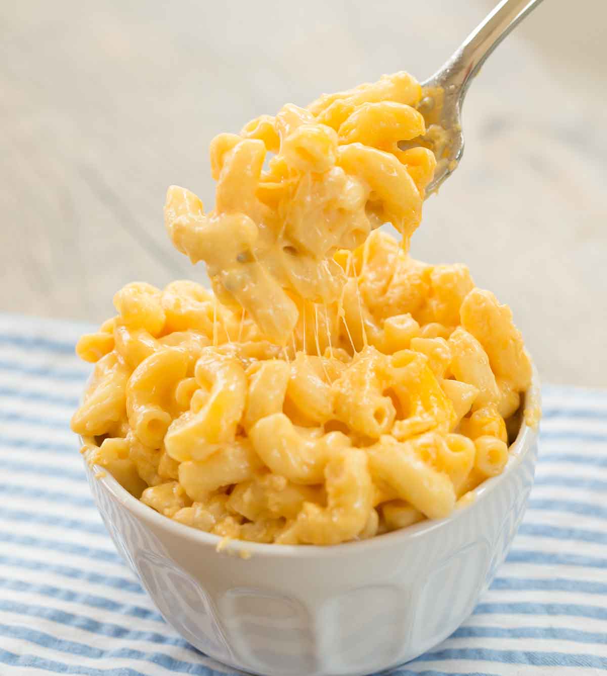 Photo of fork lifting macaroni and cheese from a white bowl, with melted cheese strings pulling.