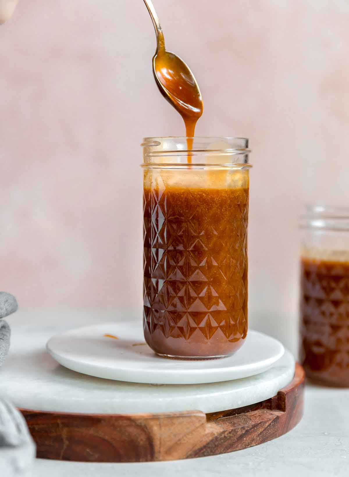 A jar of salted caramel sauce with a spoon pulling up a spoonful of caramel sauce.