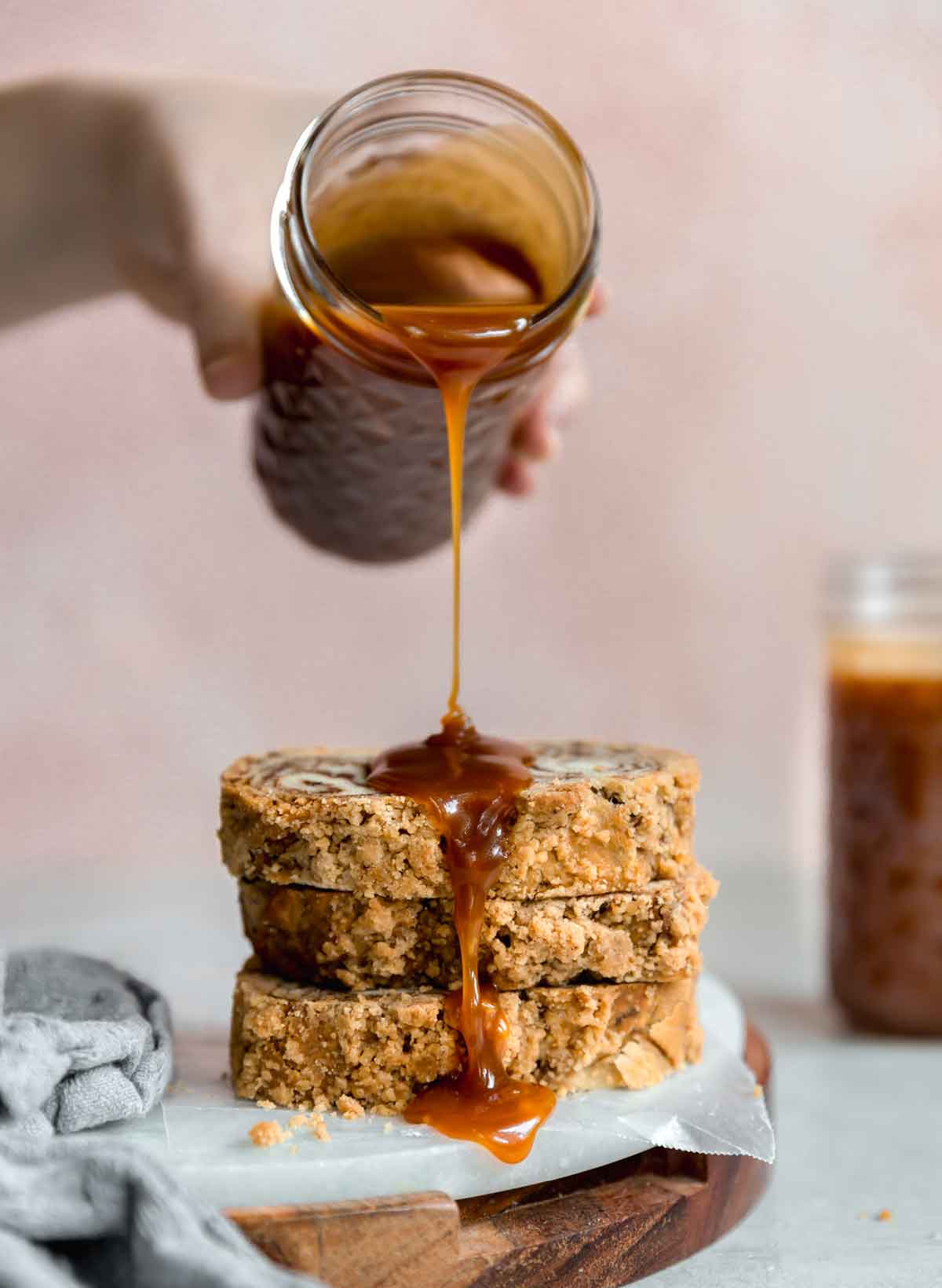 A jar of salted caramel sauce being drizzled on a stack of three slices of crumb cake.
