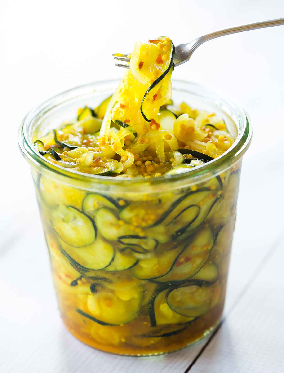 Glass jar filled with zucchini pickles and a fork pulling one out.