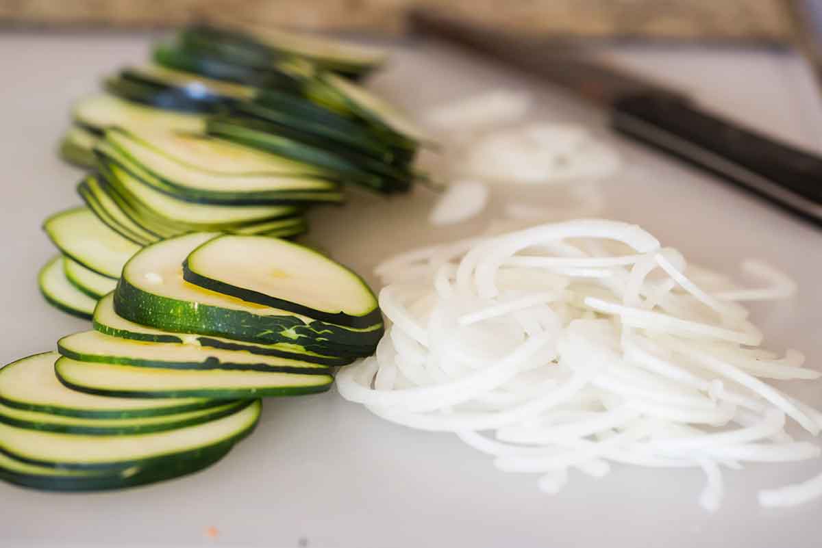 Sliced zucchini and onion on a cutting board.
