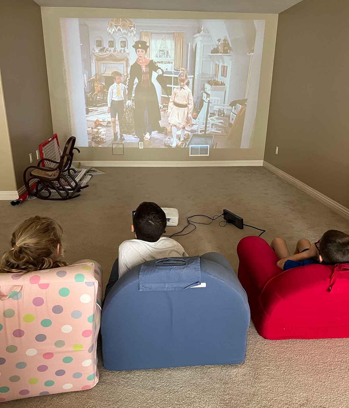 Three kids sitting in small chairs watching Mary Poppins on a projector screen.