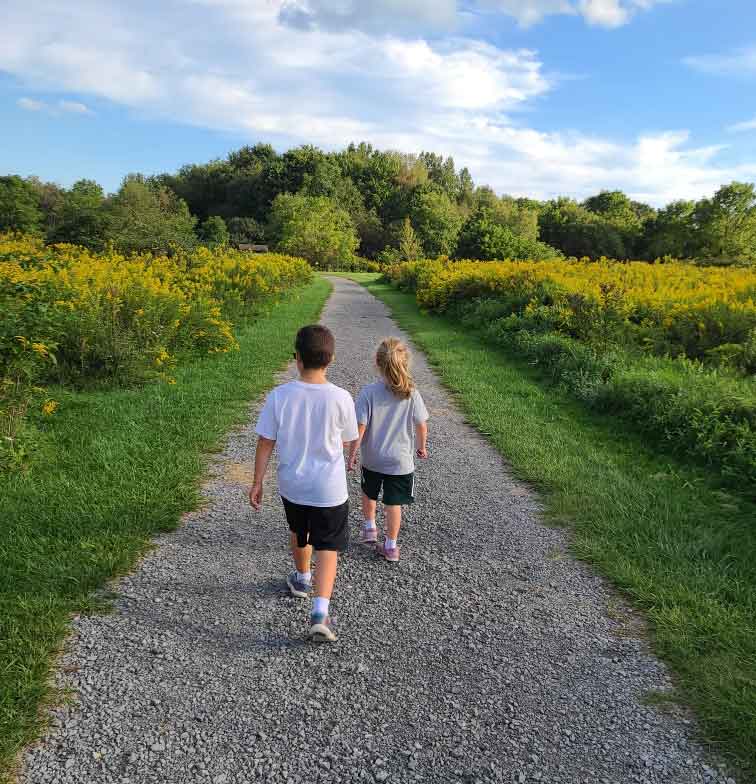 Boy and girl walking on a gravel trail surrounded by a field.
