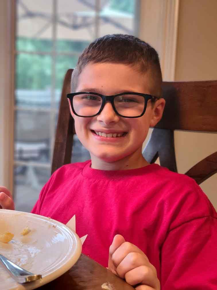 Boy with black glasses sitting in a chair at a dinner table.