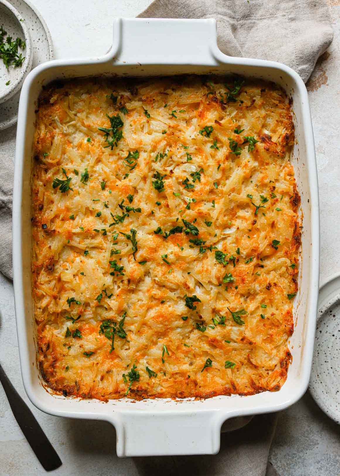 Overhead photo of hashbrown casserole in a white casserole dish, garnished with fresh parsley.