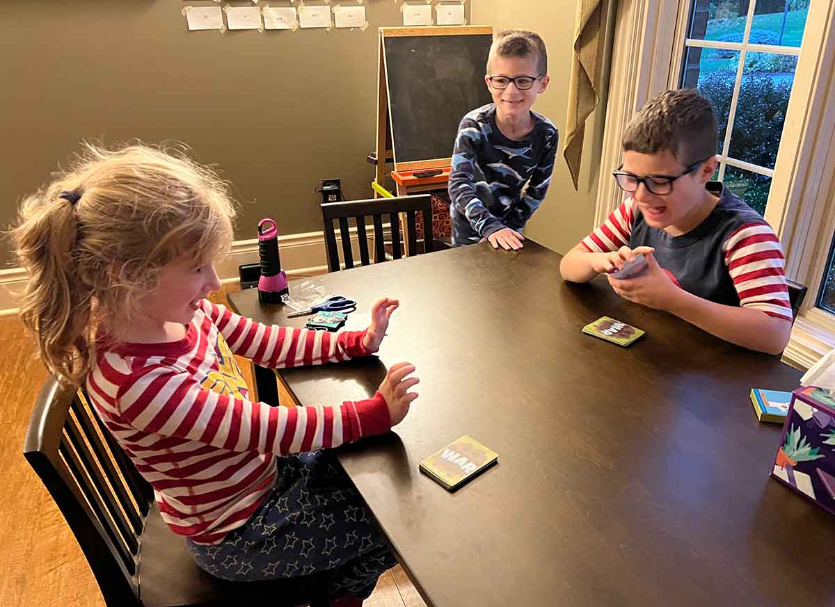 Three kids sitting around a small table playing war.