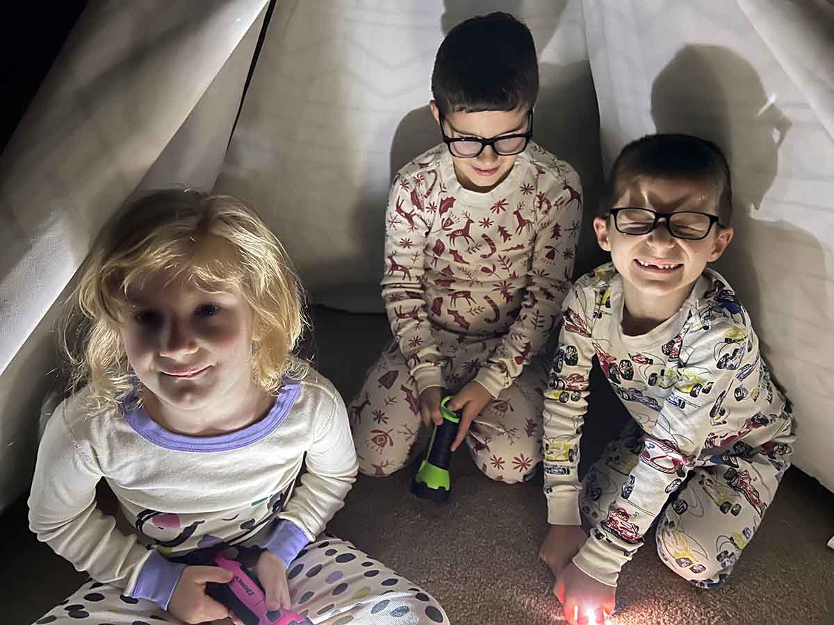 Three children in a dark tent with flashlights.