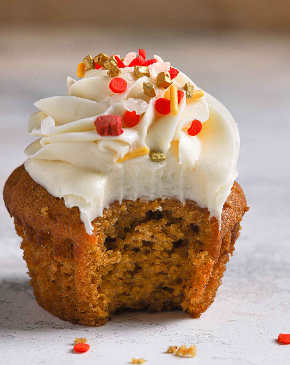 Pumpkin cupcake with cream cheese frosting with a bite taken out of it.