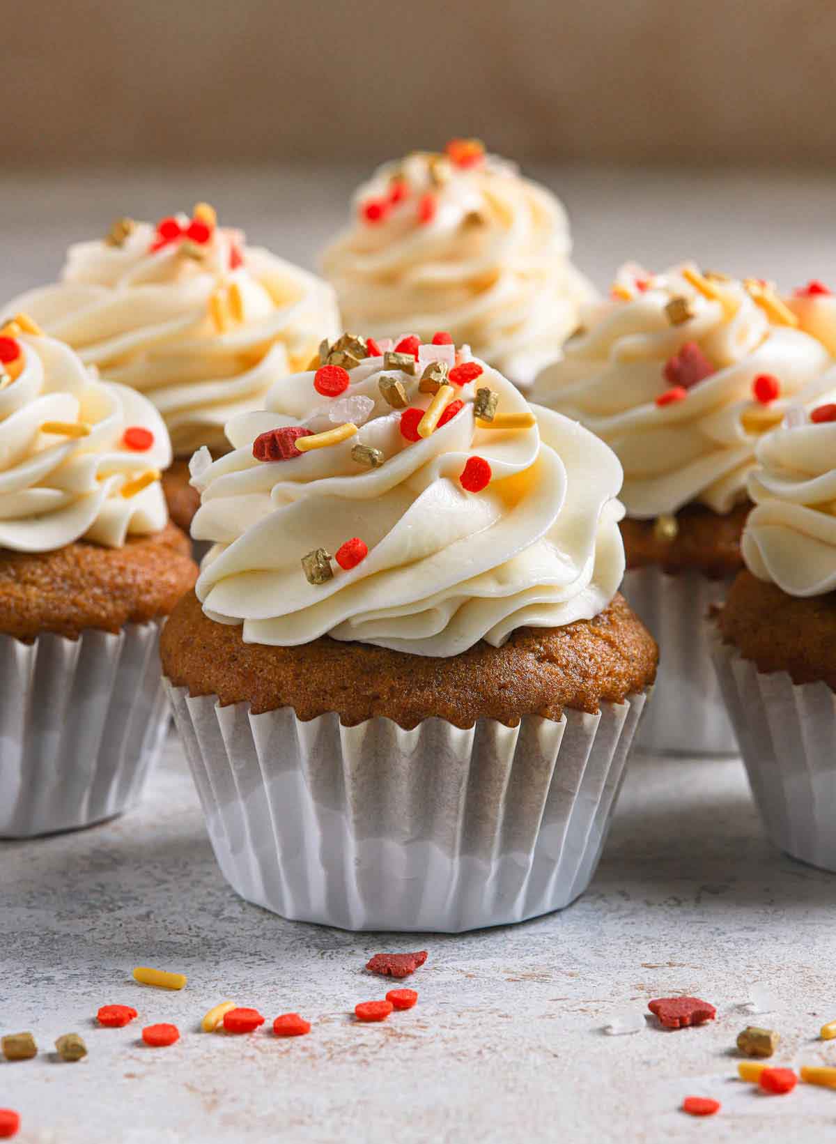 Pumpkin cupcakes in white liners topped with cream cheese frosting and fall-themed sprinkles.