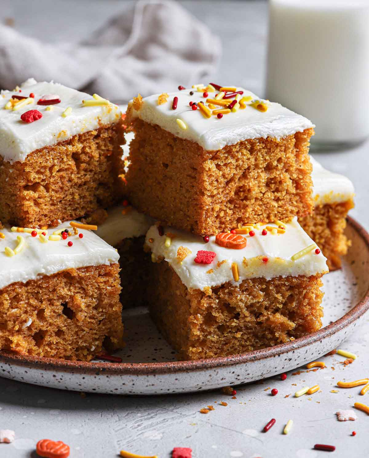 Pumpkin bars with cream cheese frosting and autumn-themed sprinkles on a white speckled plate.