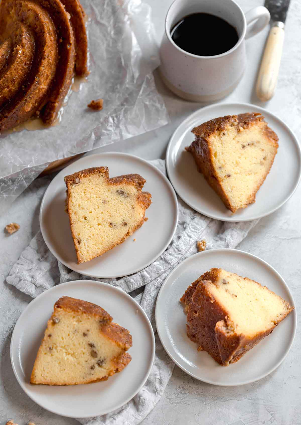 Four slices of rum cake on white plates with a cup of coffee in the background.